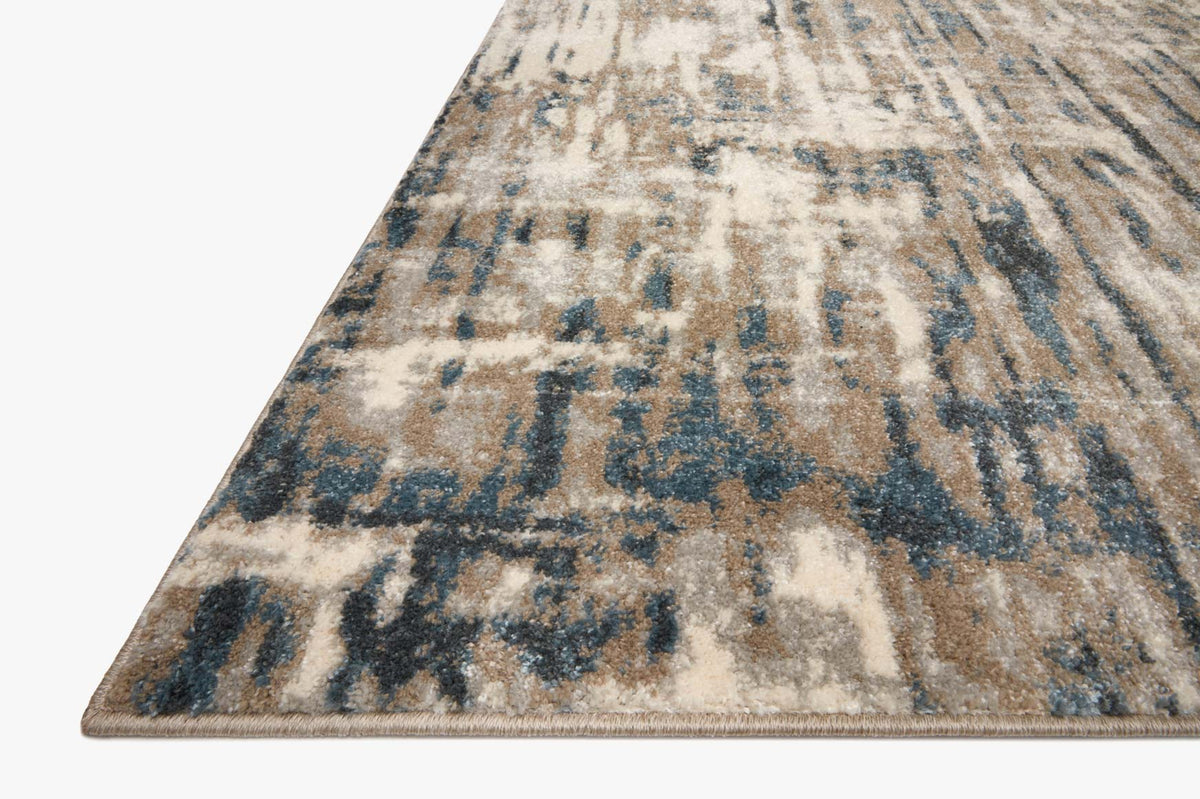 Corner view of distressed abstract rug with blue and stone pattern and bound edge
