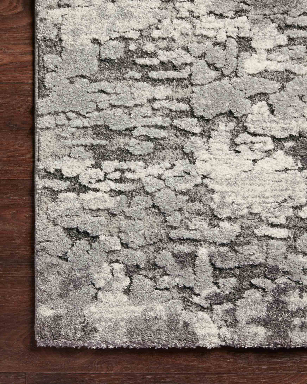 Charcoal and grey power-loomed rug with abstract distressed pattern, against dark wood floor.