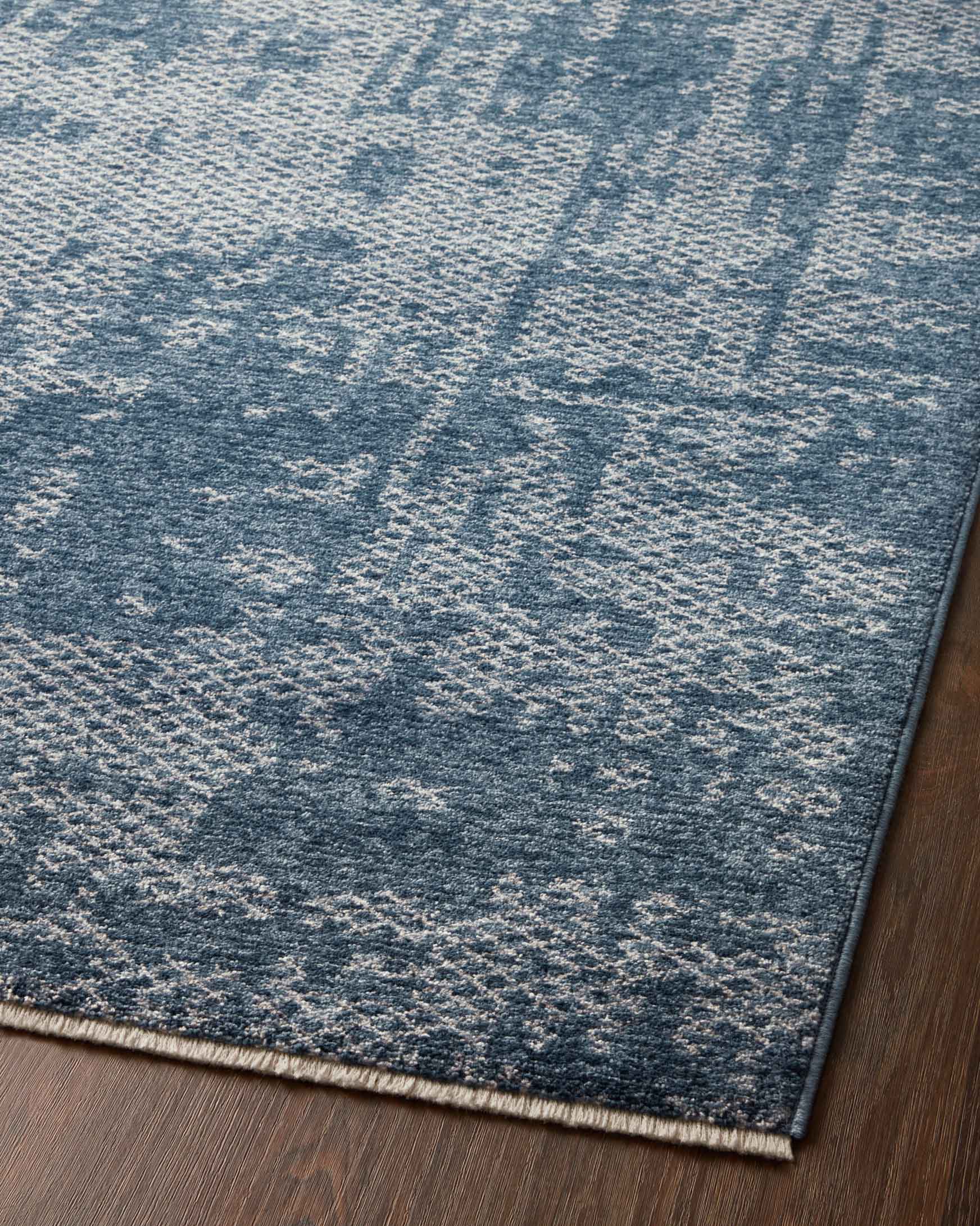 Denim blue rug with dove geometric pattern and short fringe border on hardwood floor