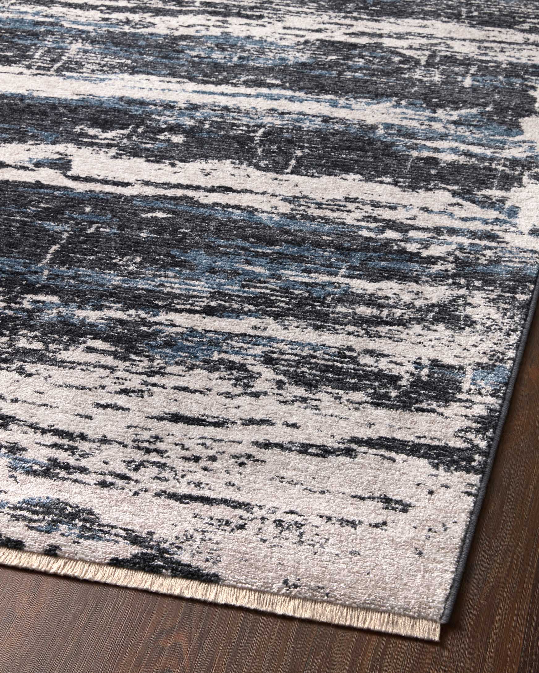 Charcoal and dove rectangular rug with distressed stripes, angled on hardwood floor.