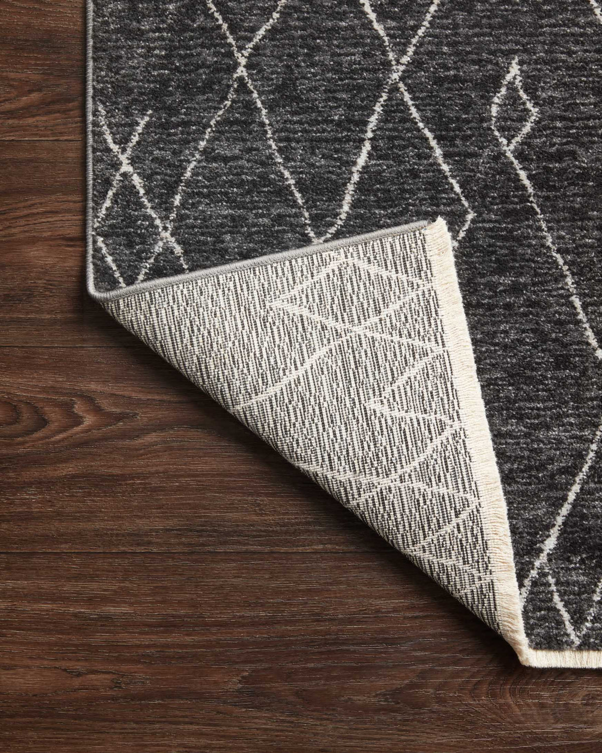 Charcoal rug rolled back on wood floor, showing underside and white pattern