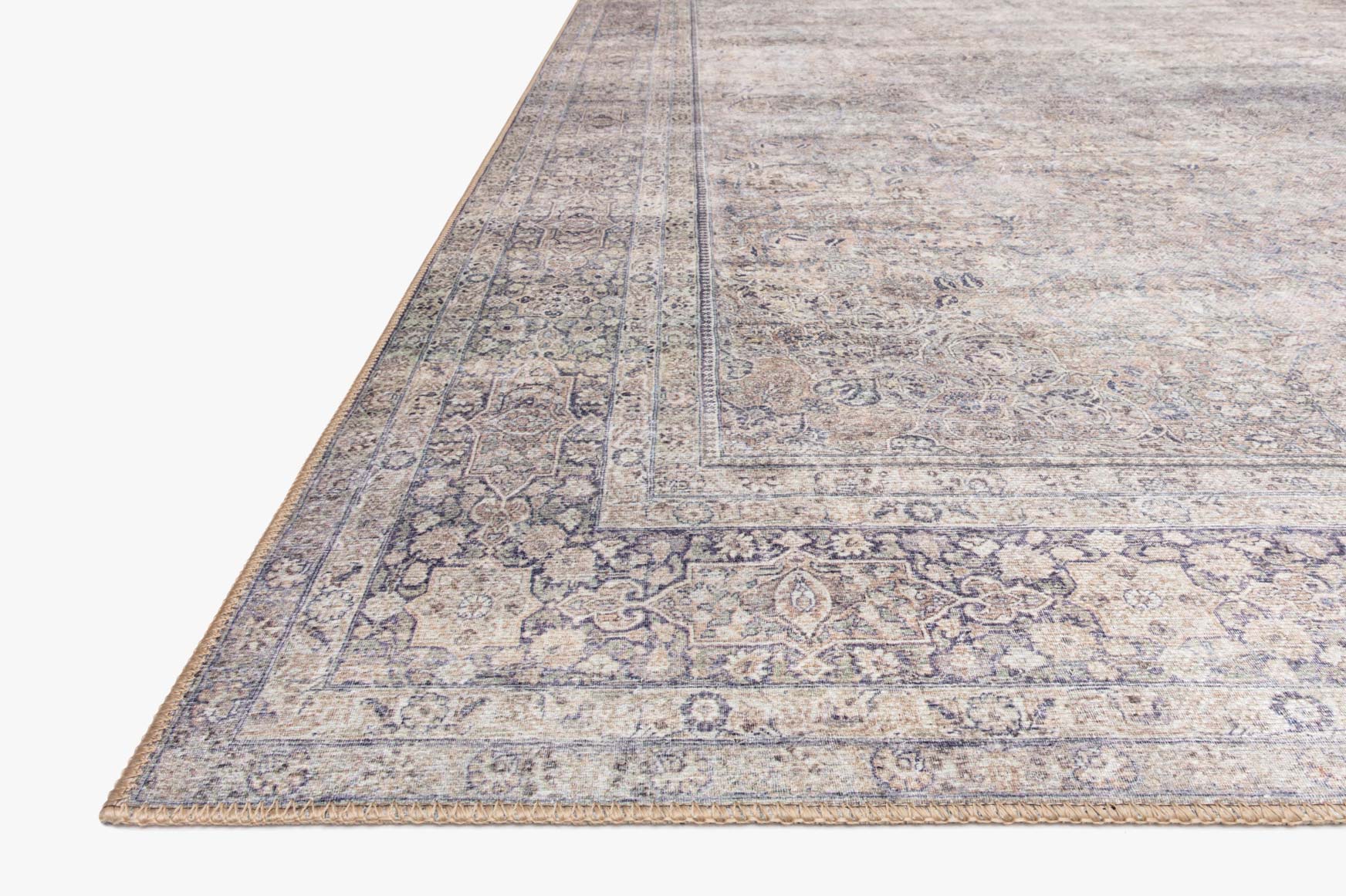 Close-up corner of a silver and charcoal rug with ornate motifs and patterned border.