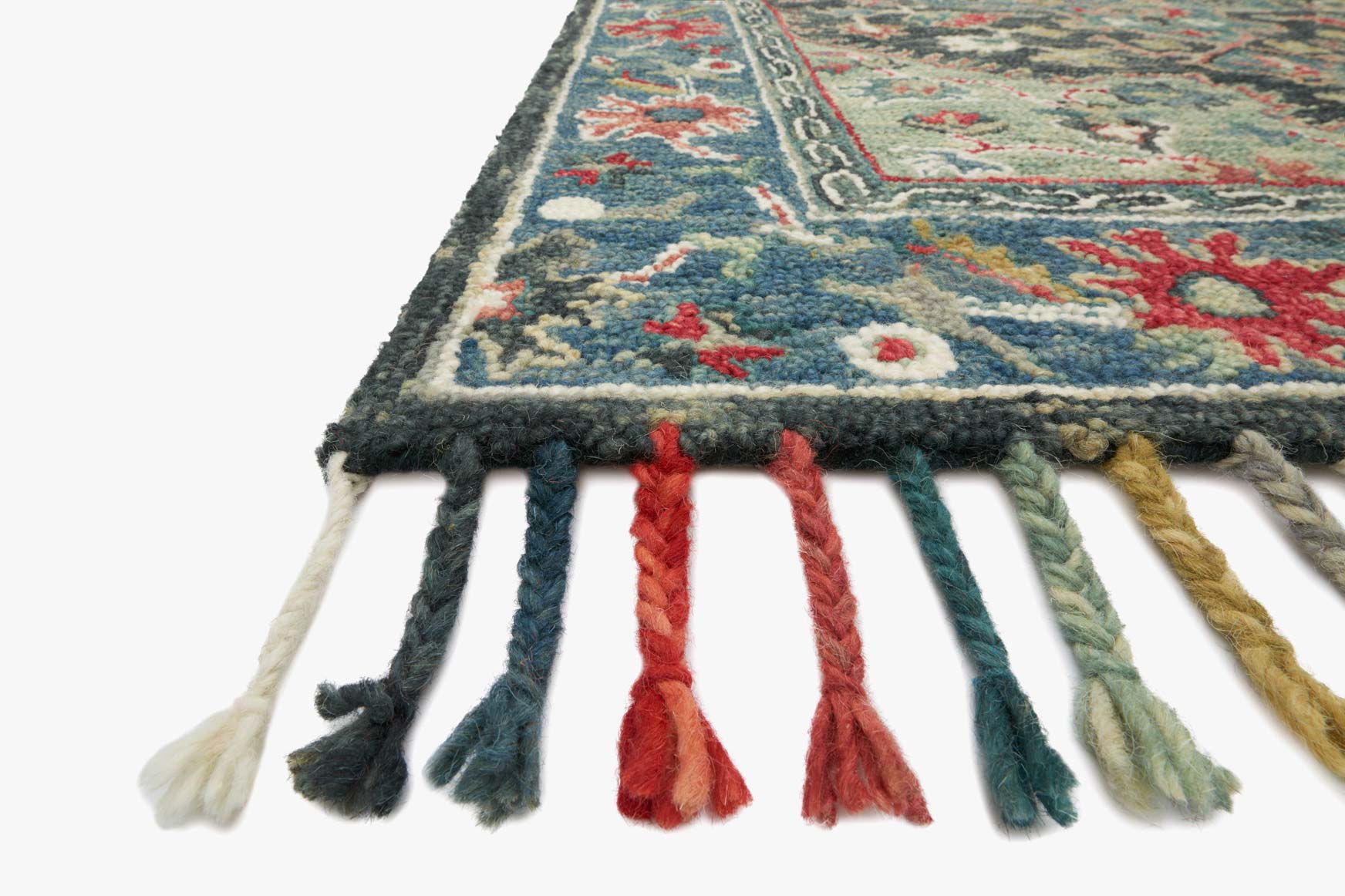 Transitional hooked rug corner with blue border, colorful motifs, and multi-color tassel fringe