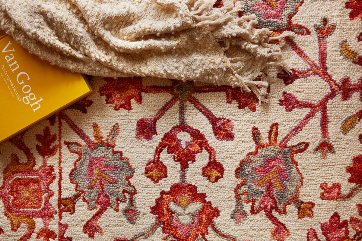 Close-up of hooked rug texture with off-white ground and berry red floral motifs