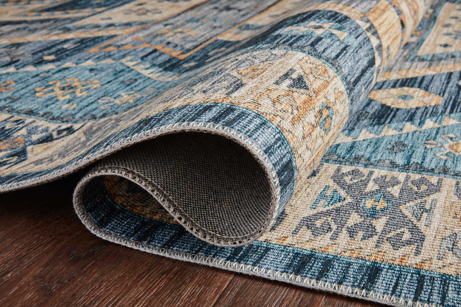 Rolled edge detail of blue and gold geometric rug with visible textured weave
