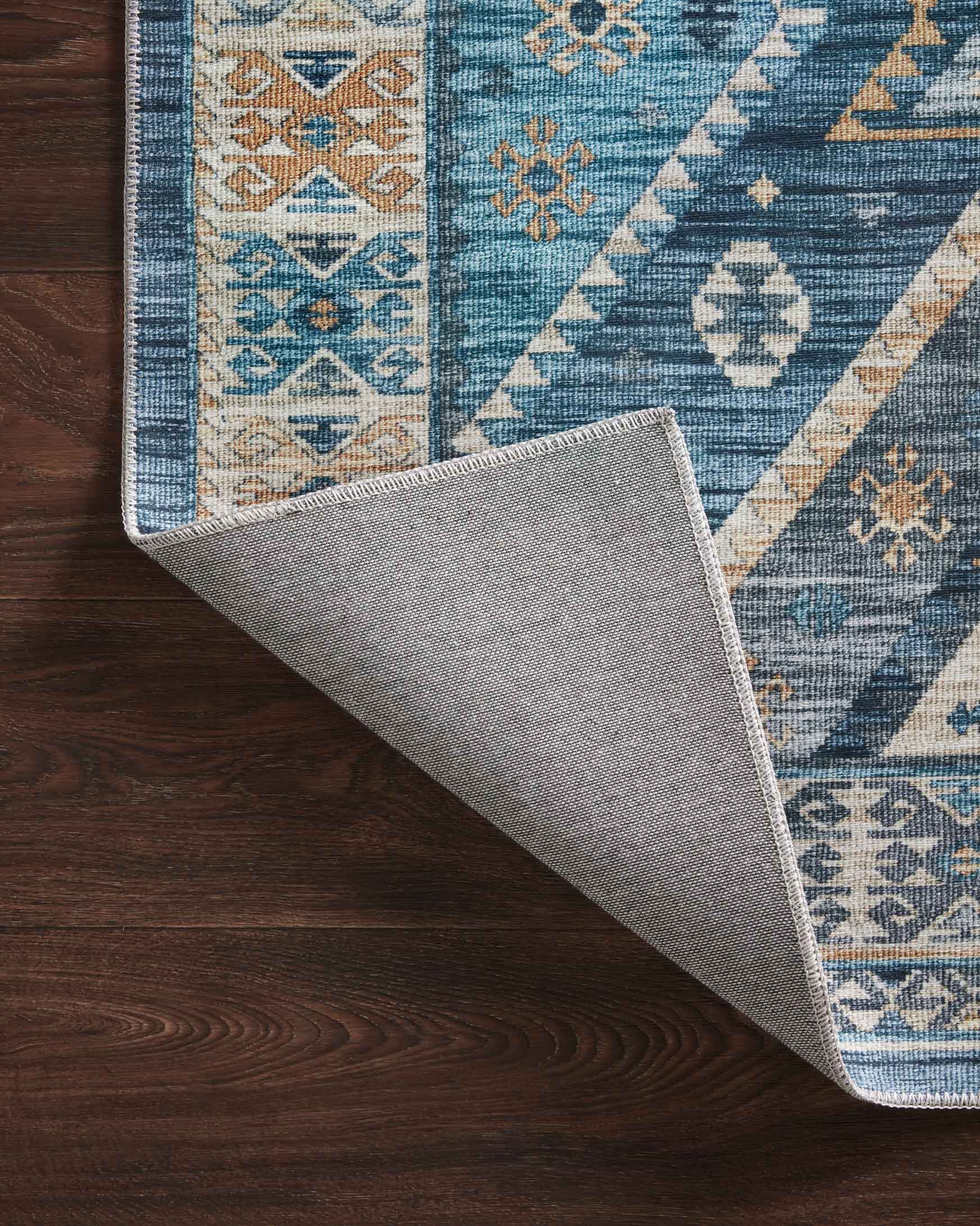 Rug corner flipped to show light gray backing on a blue and gold geometric design