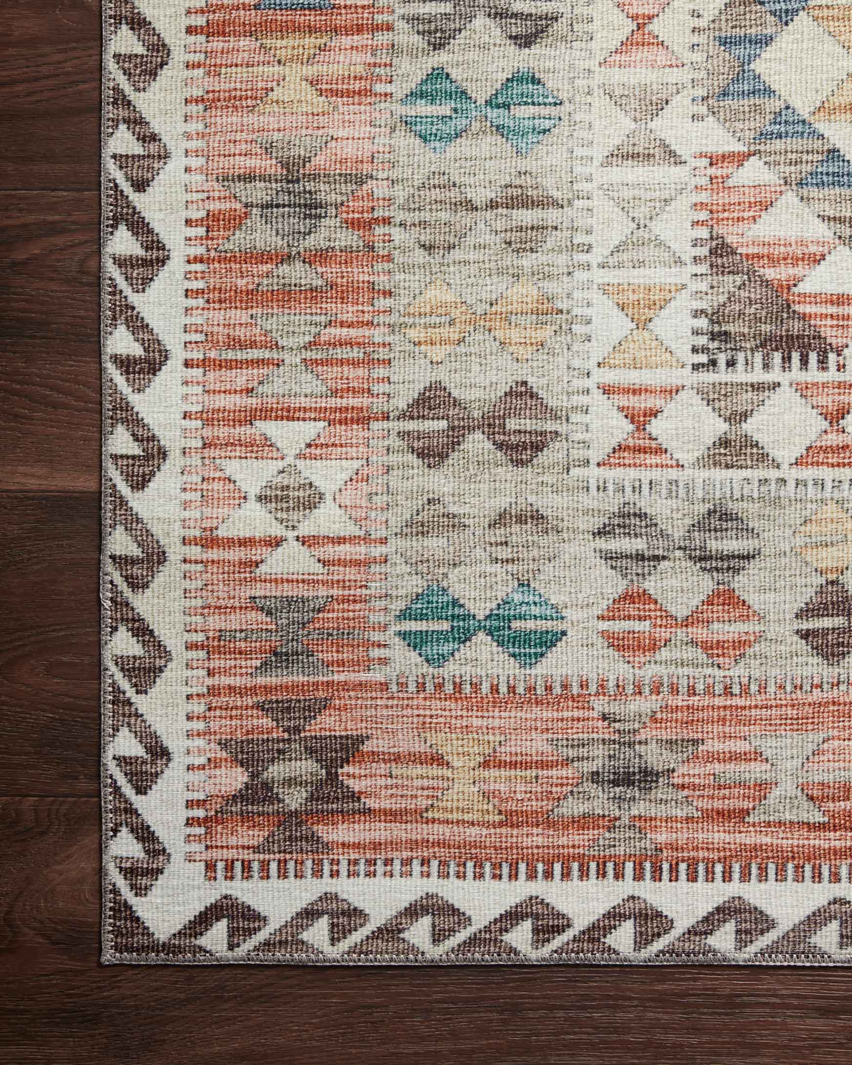 Close-up of rug border with repeating geometric motifs in ivory, rust, teal, and gray.
