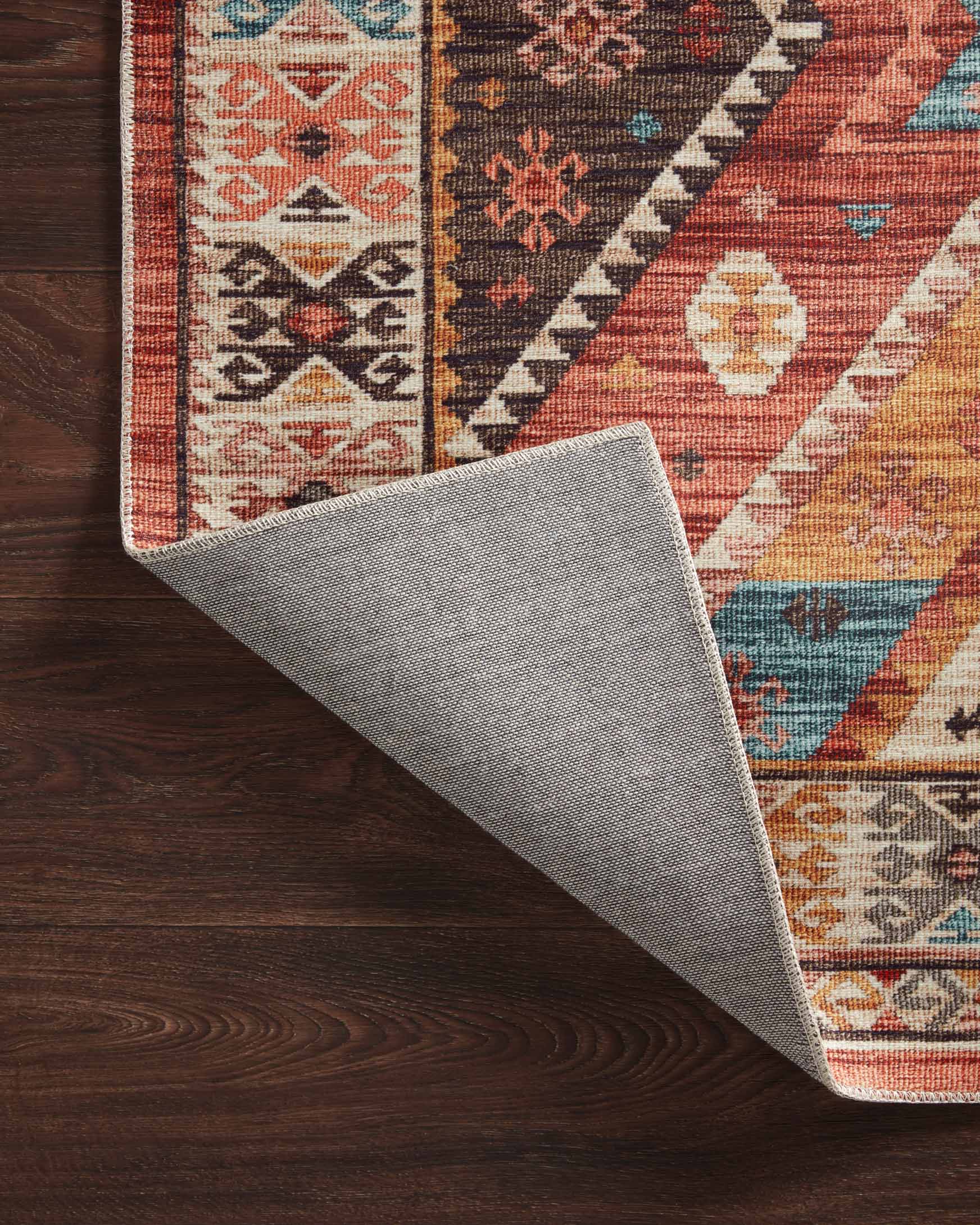 Folded edge of geometric rug on dark wood floor with red, teal, and cream design
