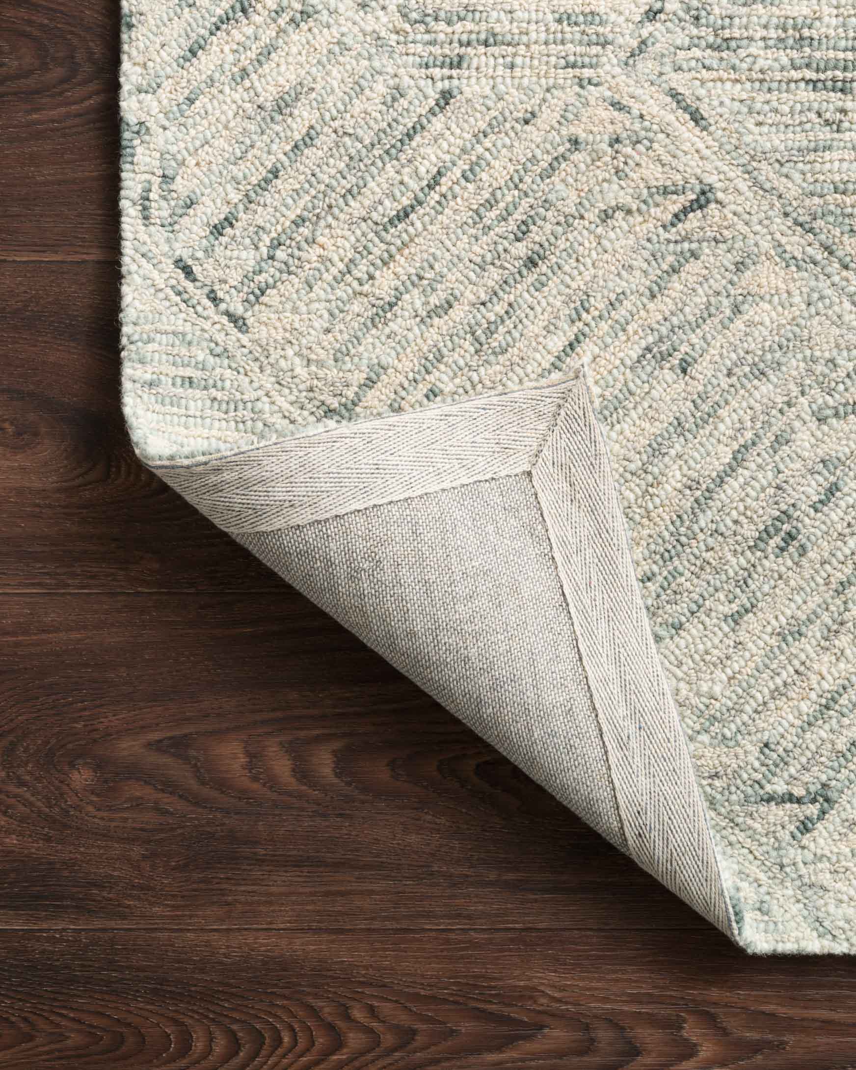 Hand-tufted rug edge with bound backing and sky-blue geometric pattern on textured pile
