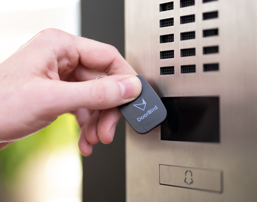 Hand holding DoorBird RFID key fob for access, dark gray