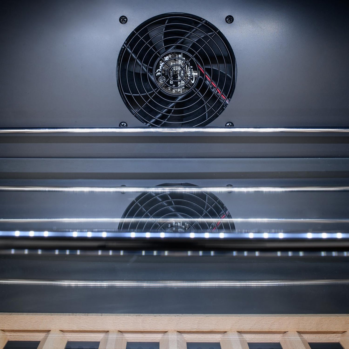 Beverage cooler interior with circulation fans and vent grilles above shelves