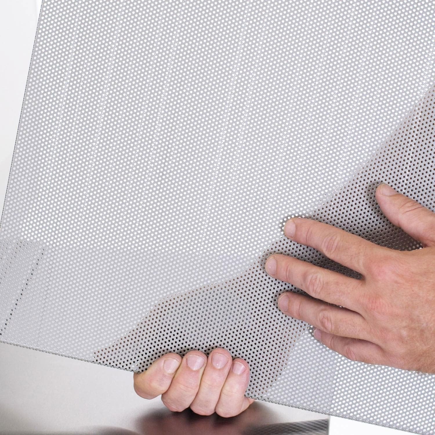 Hands fitting a perforated mesh flame guard drip tray into a grill opening