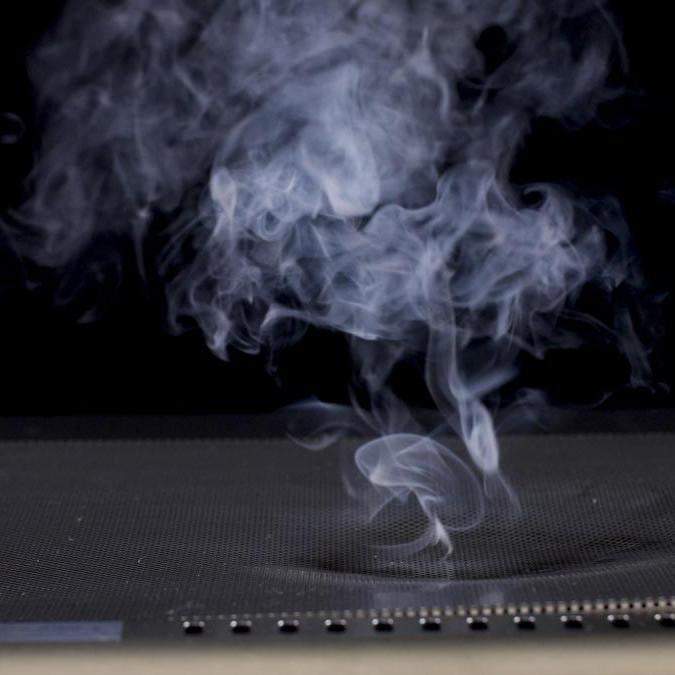 Perforated metal drip tray flame guard with vent holes, shown in use with smoke