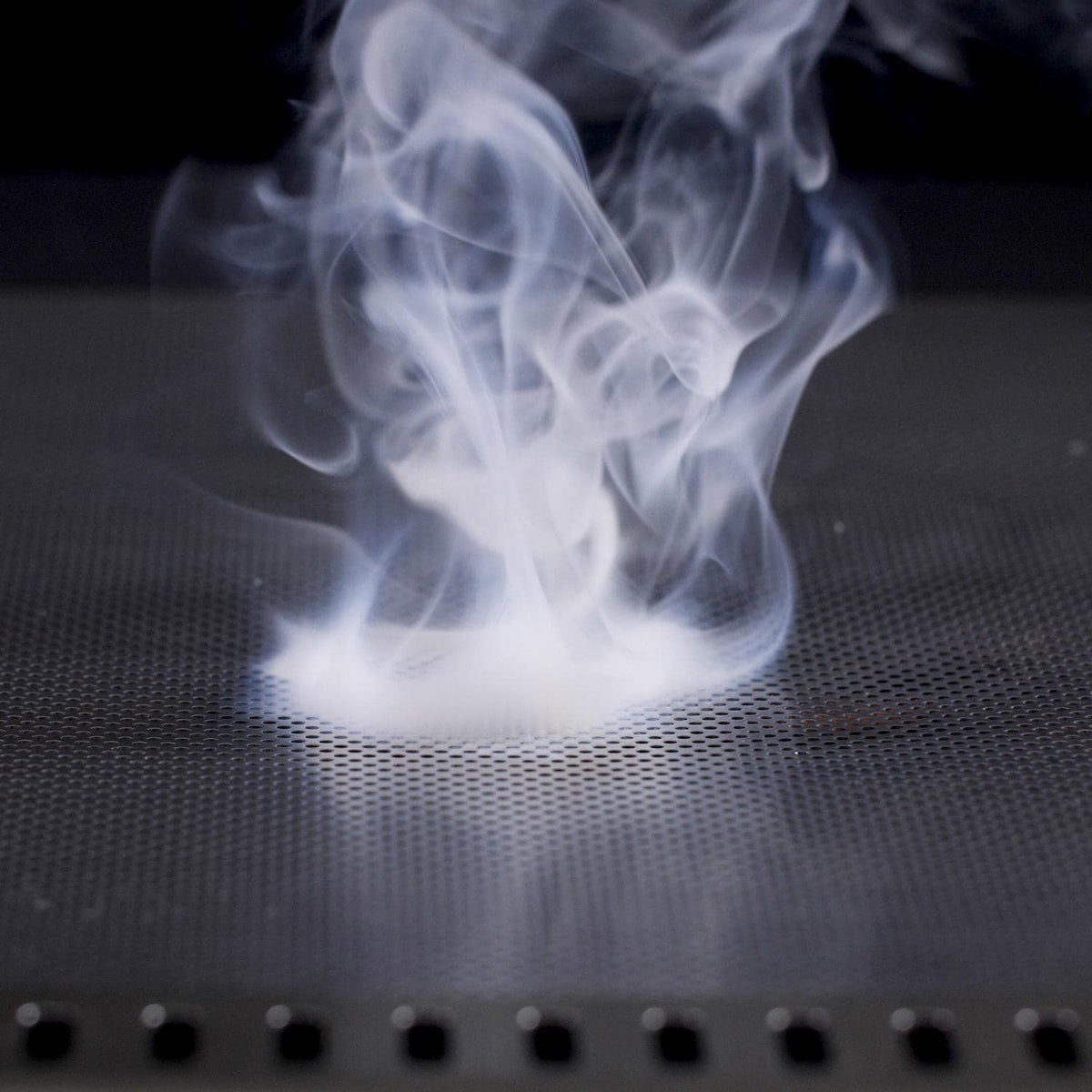 Flame guard drip tray with perforations, smoke rising above the metal