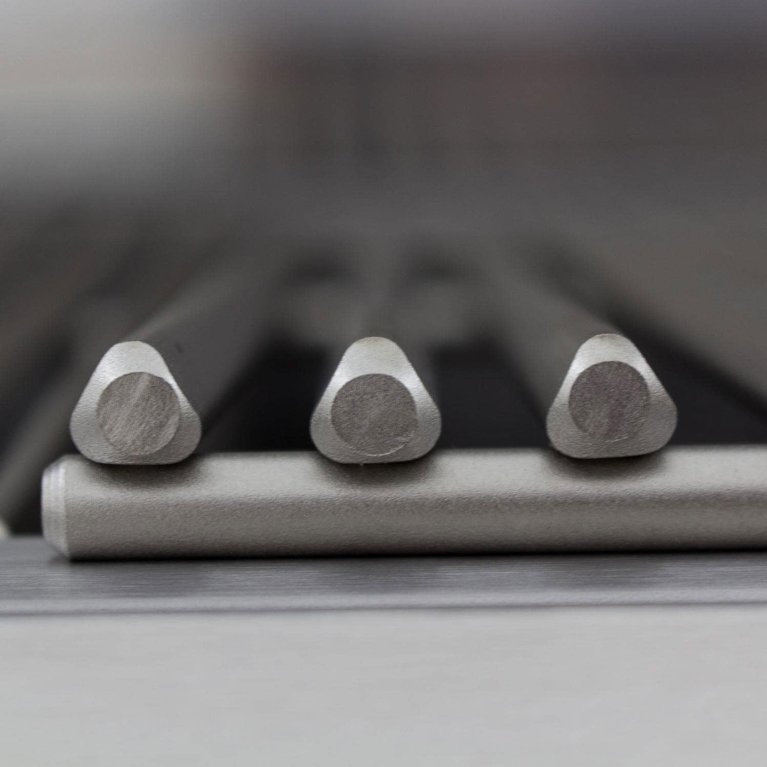 Three stainless steel burner control knobs with textured grips on a dark panel