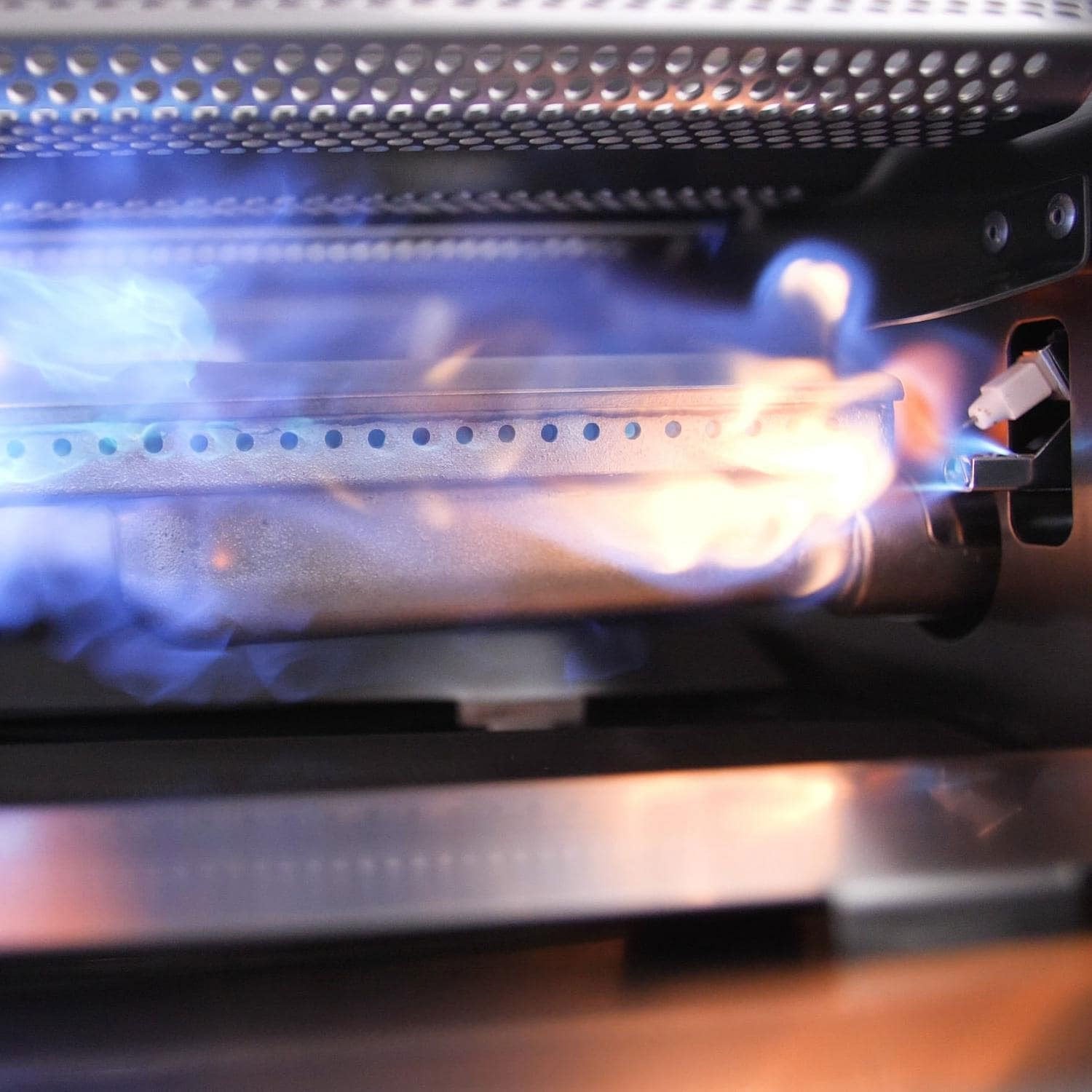 Gas grill burner with blue flame and glowing burner ports