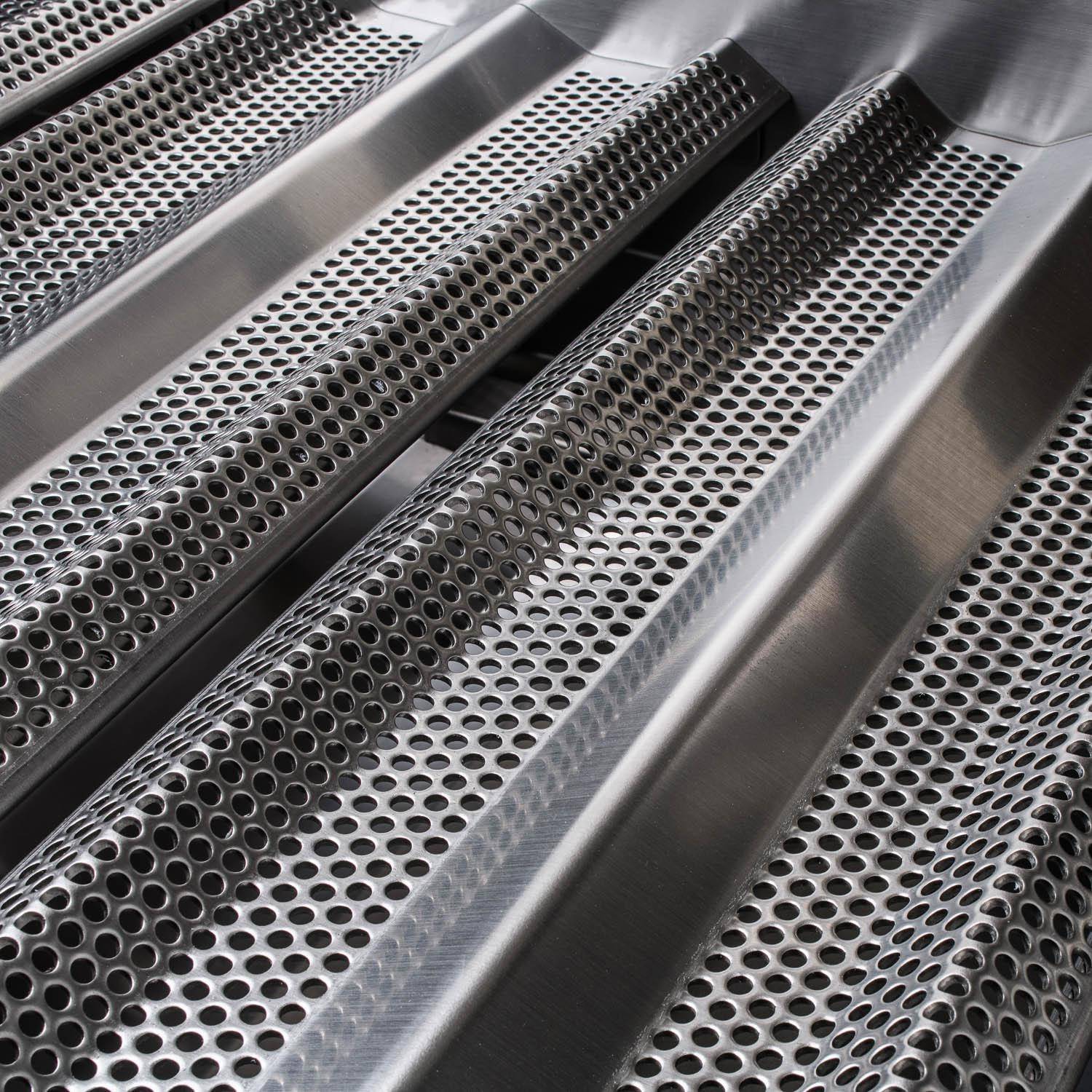 Close-up of stainless flame tamers with round perforations along the grill