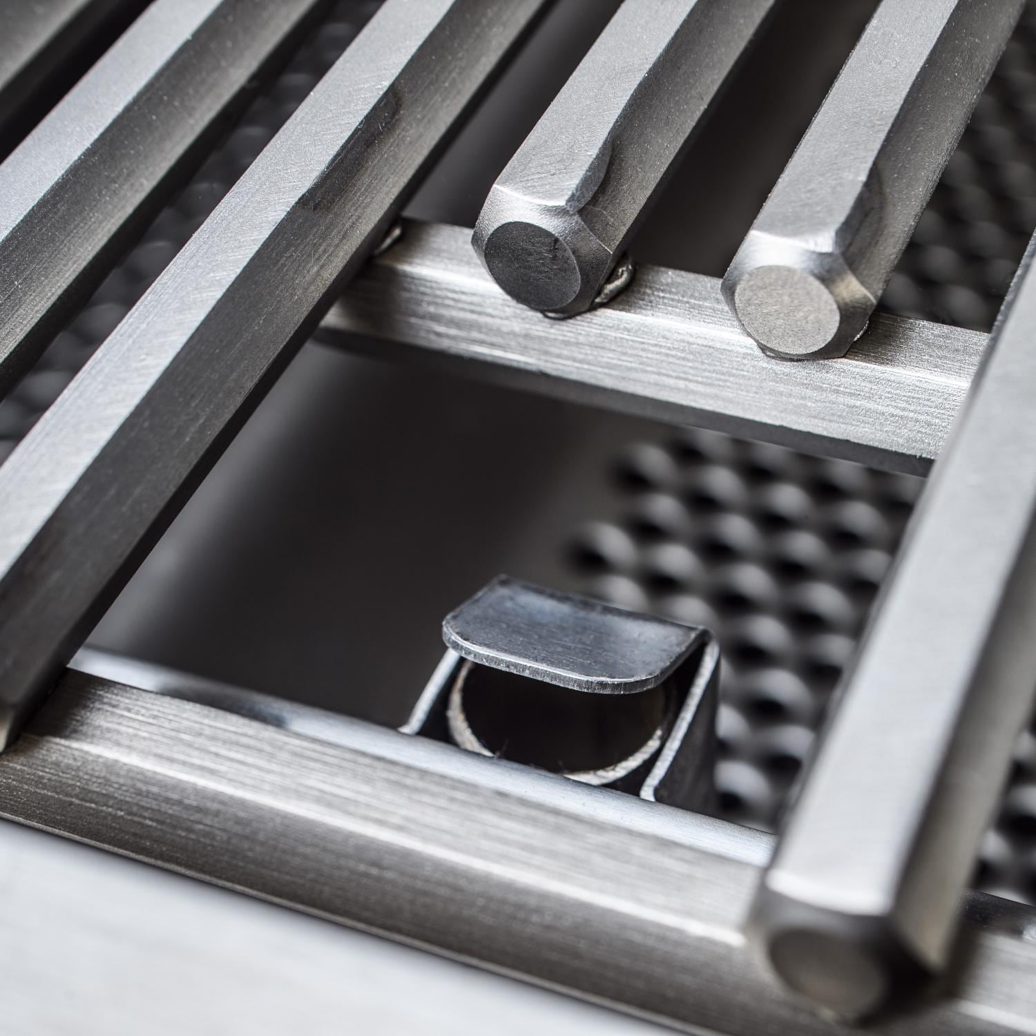Open grill burner area with metal briquette-style bars and dark burner openings