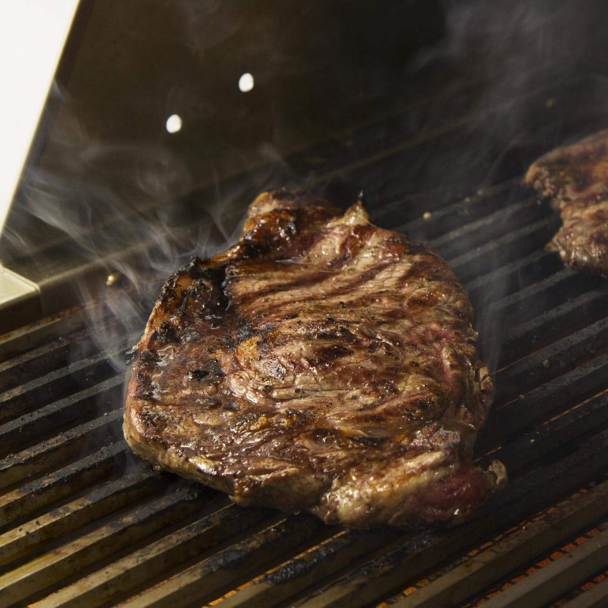 Sear-ready steak on infrared searing burner grill bars with visible smoke