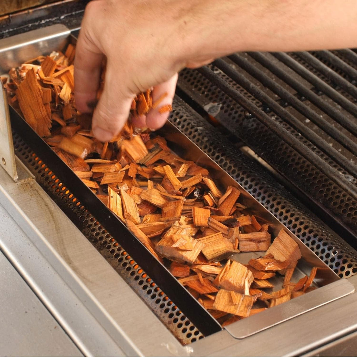 Hand loading wood chips into stainless steel smoker box tray