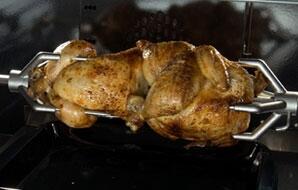 Gas range rotisserie holding roasted whole chicken on spit rods
