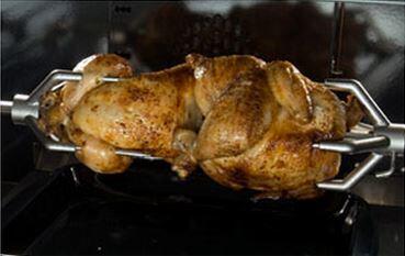 Rotisserie chicken roasting on a gas range spit inside the oven