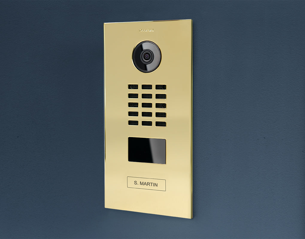 Brass IP video door station mounted on wall with camera lens and nameplate