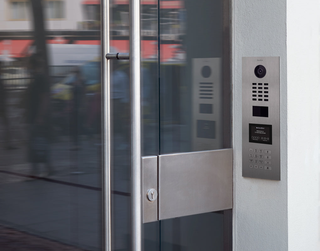 Stainless steel video door station mounted beside glass door with keypad and camera