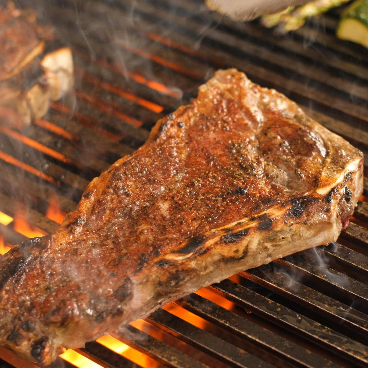 Seasoned steak grilling on stainless grate with orange flame glow