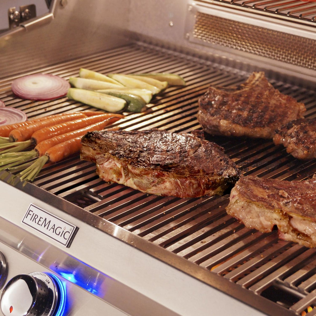 Stainless steel grill cooking grate with steaks, vegetables, and blue control lights