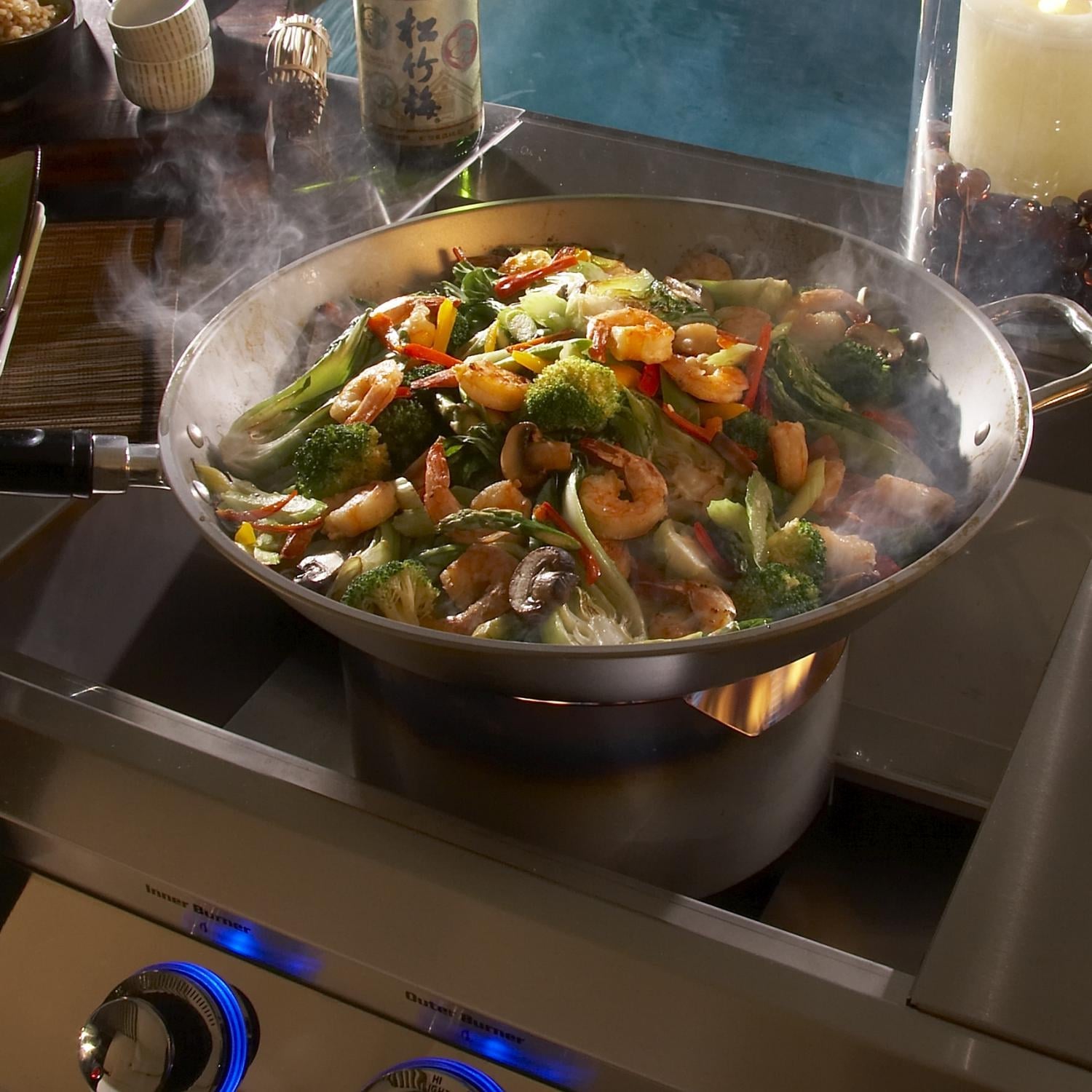 Stainless steel built-in propane burner with smoke rising under a cooking pan