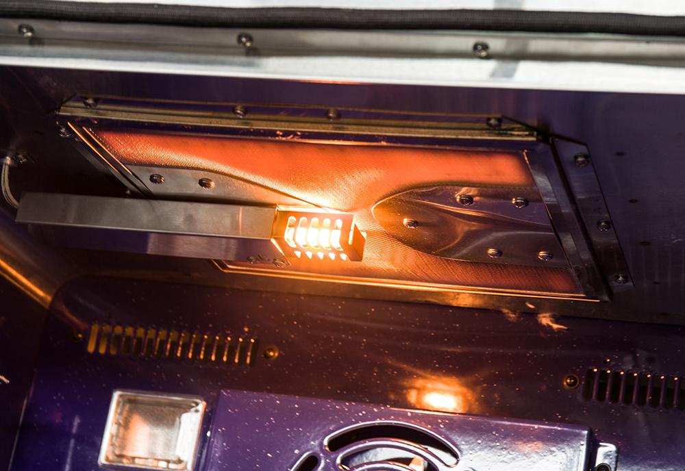 Gas oven interior with glowing burner elements and reflective back panel