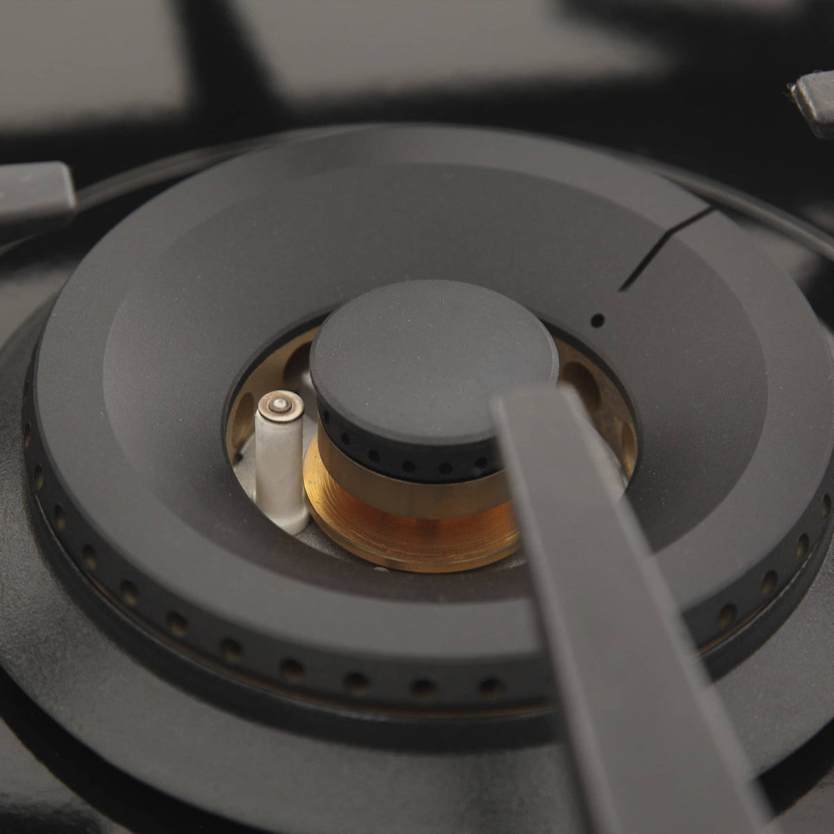 Round gas burner cap and ignition ring on black stovetop grate, close-up