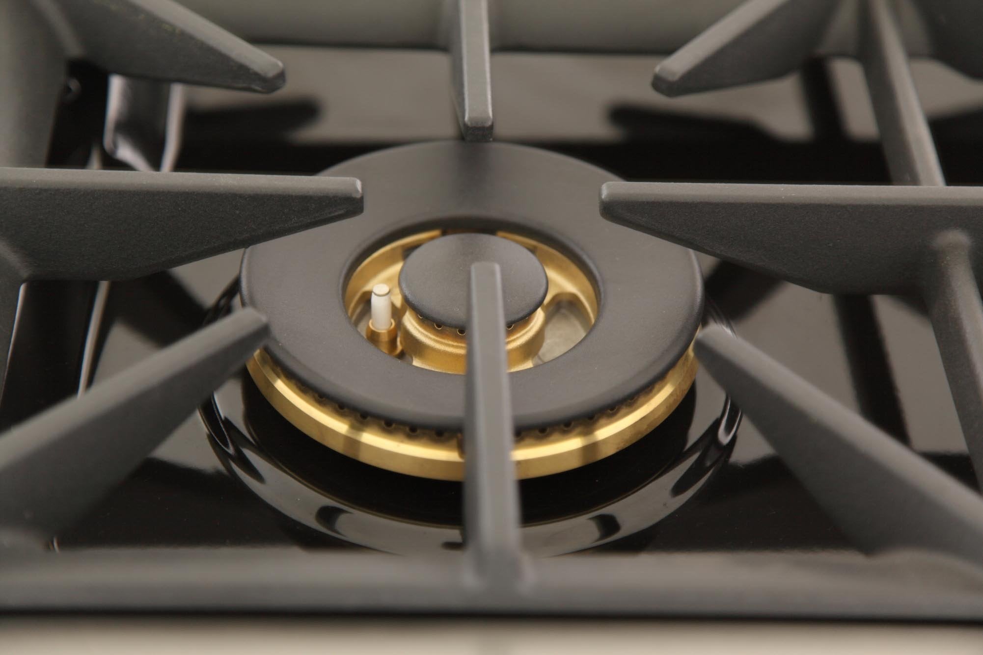 Sealed gas burner with round brass cap and black grate on range cooktop