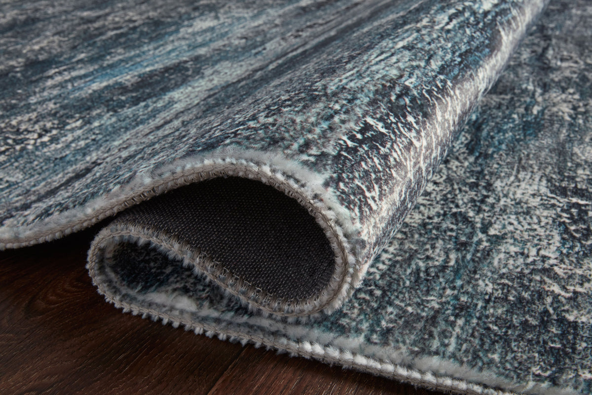 Hand-tufted rug edge showing blue-gray pile and dark backing underside