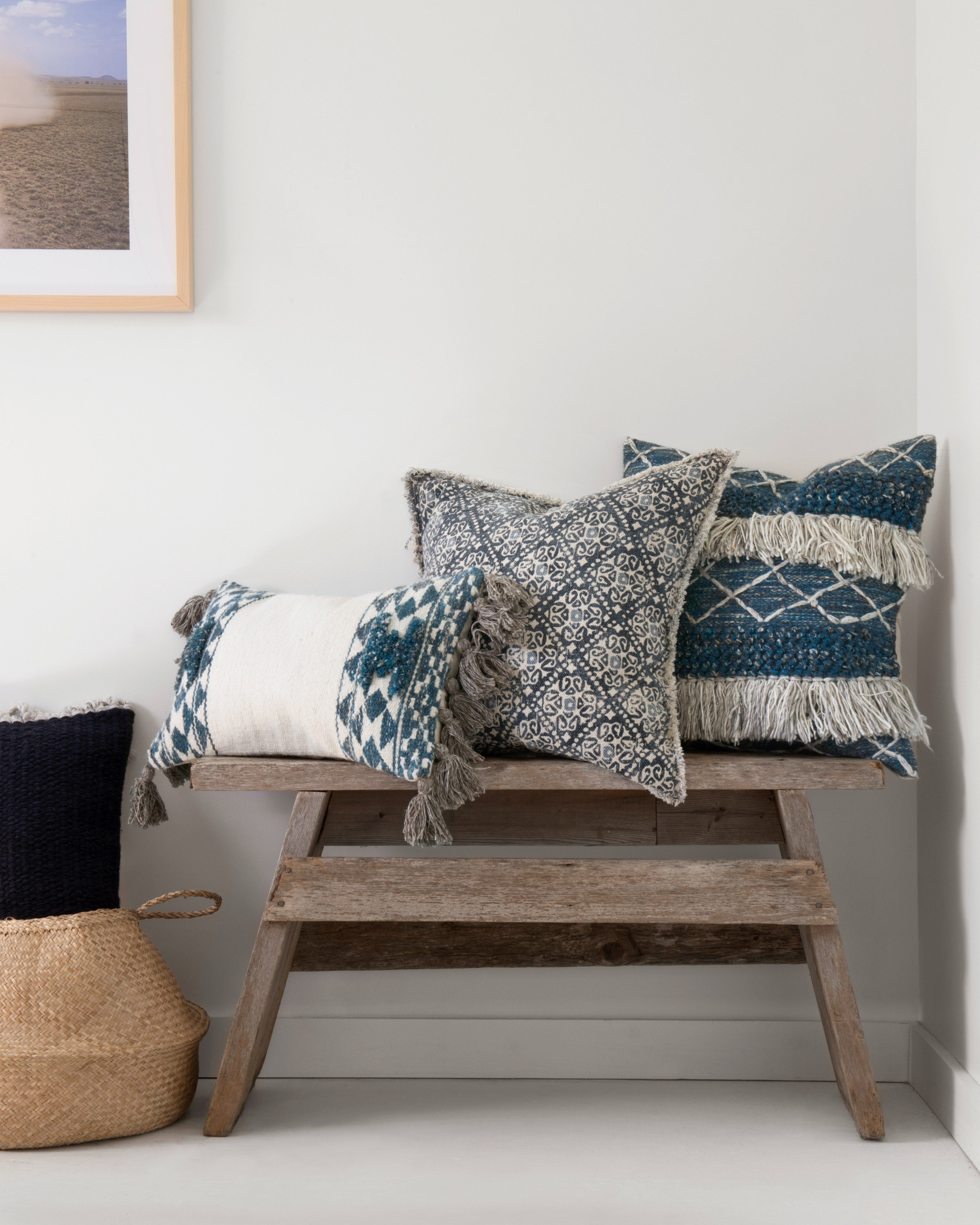 Decorative down-filled pillows on a bench, blue and cream geometric covers with fringe