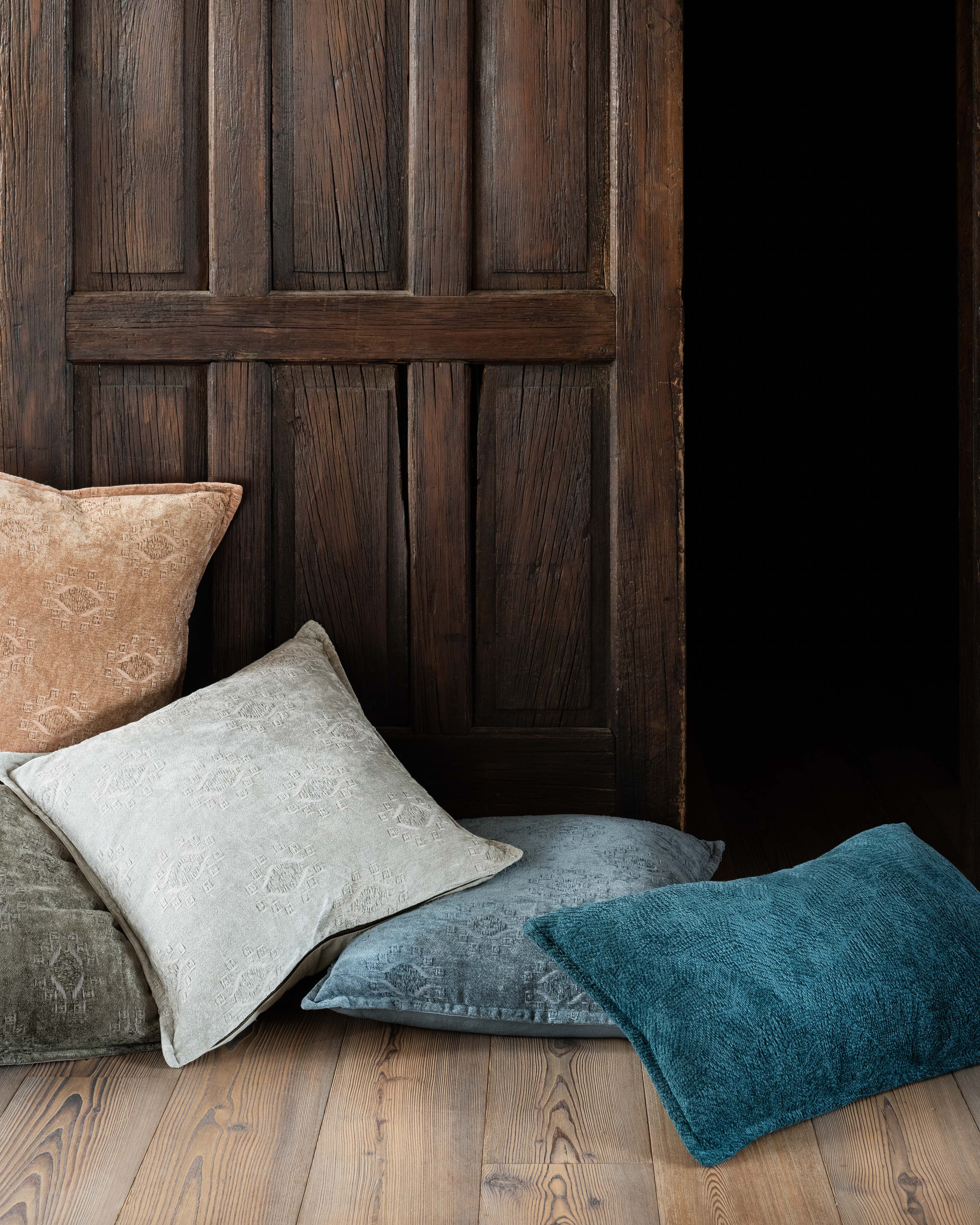 Teal down-filled decorative pillow with textured fabric, lying angled on bed