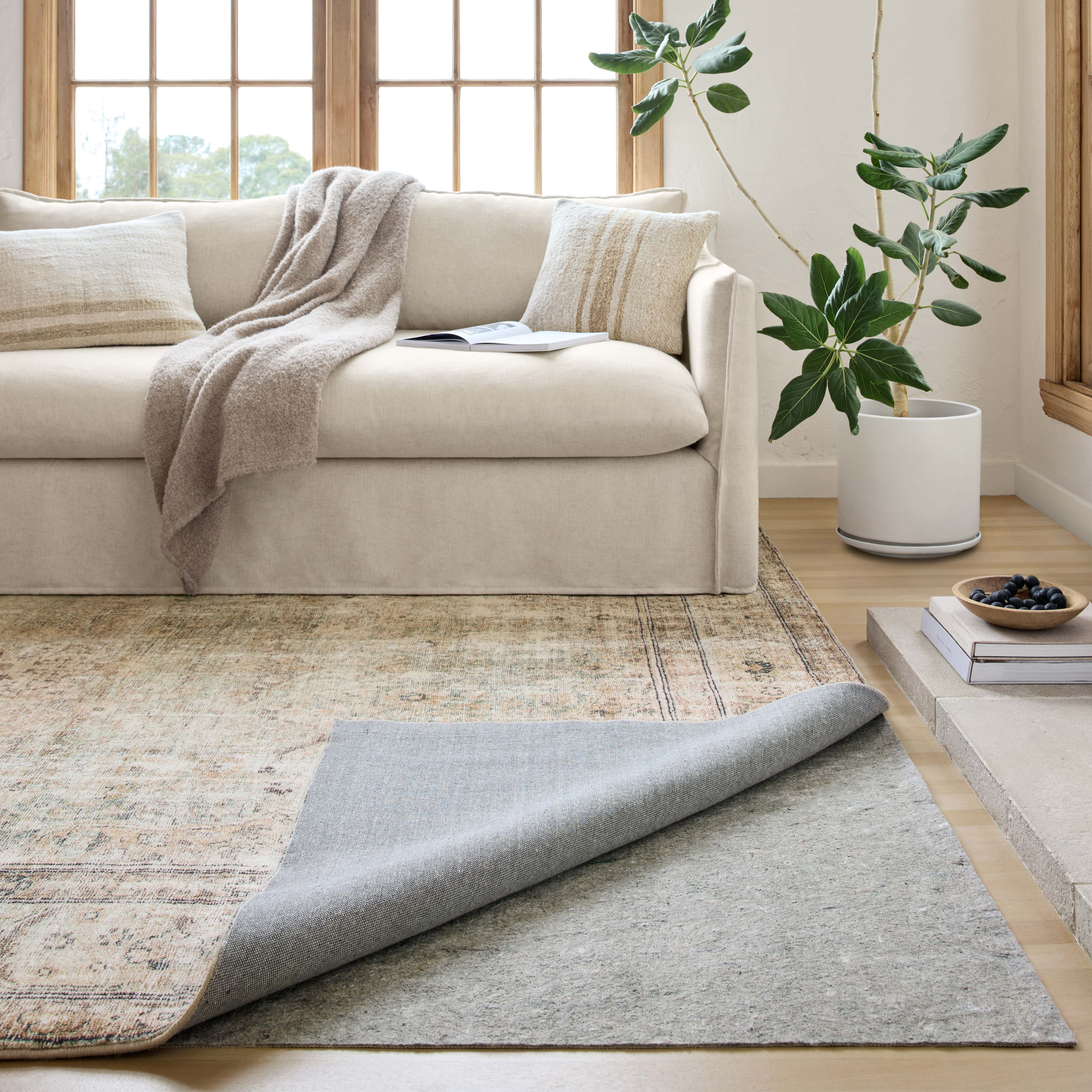 Grey rug pad with textured grip backing under an area rug on hardwood floor