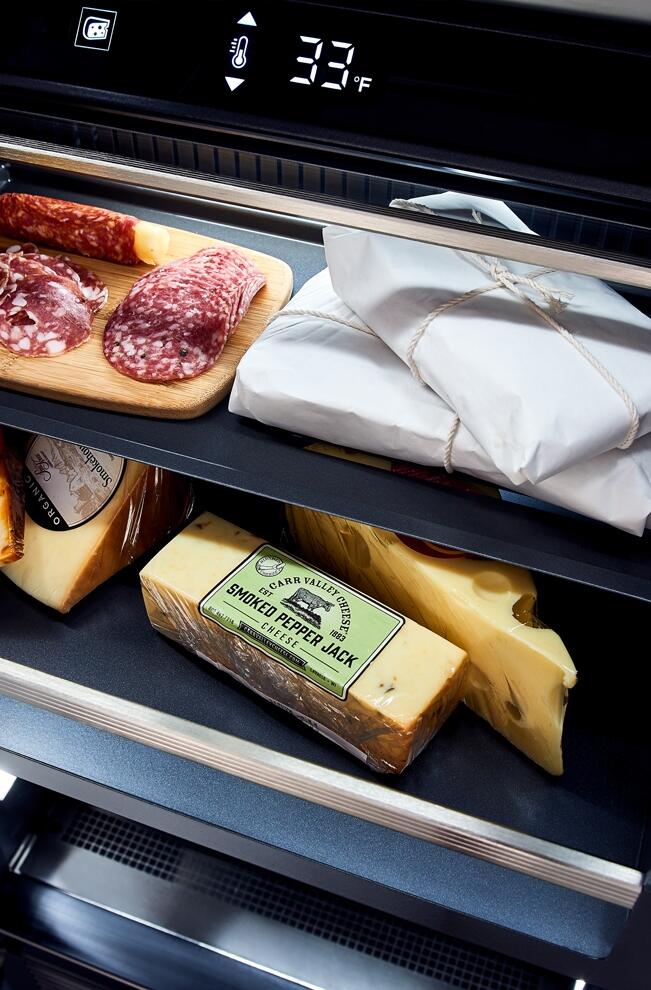 Built-in upright refrigerator with open drawers, stacked cheese and packaged meats