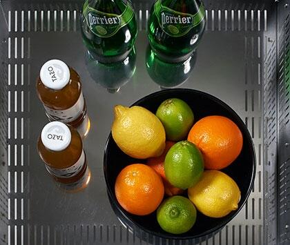 Refrigerator interior shelf with bottles and bowl of citrus fruit