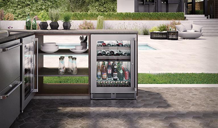 Outdoor built-in beverage center unit with glass door, stocked bottles and cans inside.