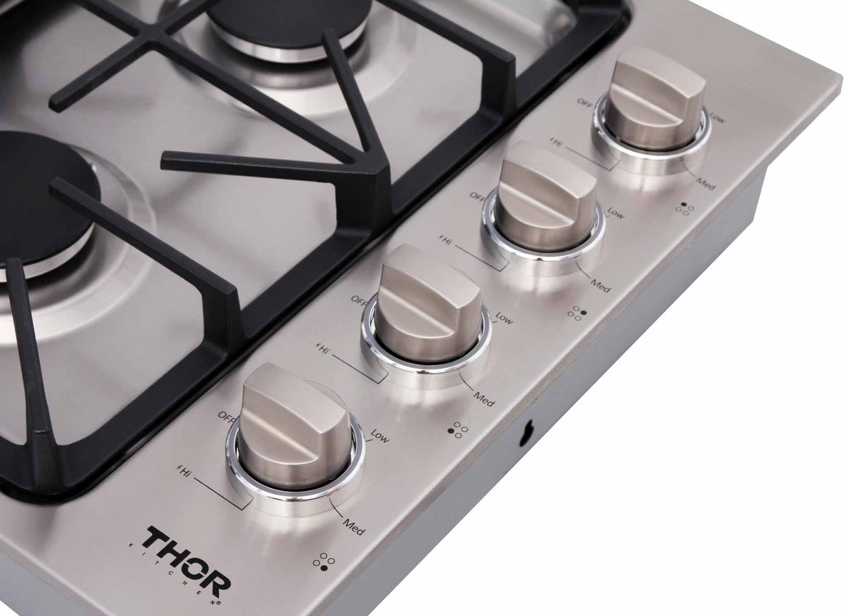 Stainless gas cooktop control panel with four round metal knobs and burner grates