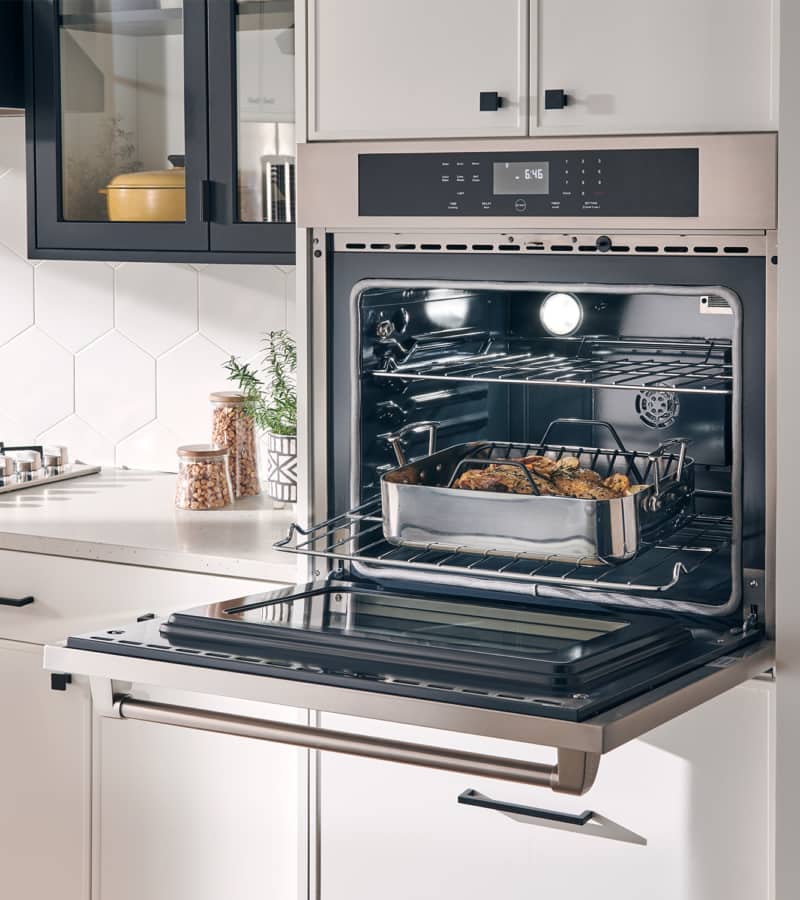 Stainless electric wall oven with open door, interior racks, and self-cleaning mode display