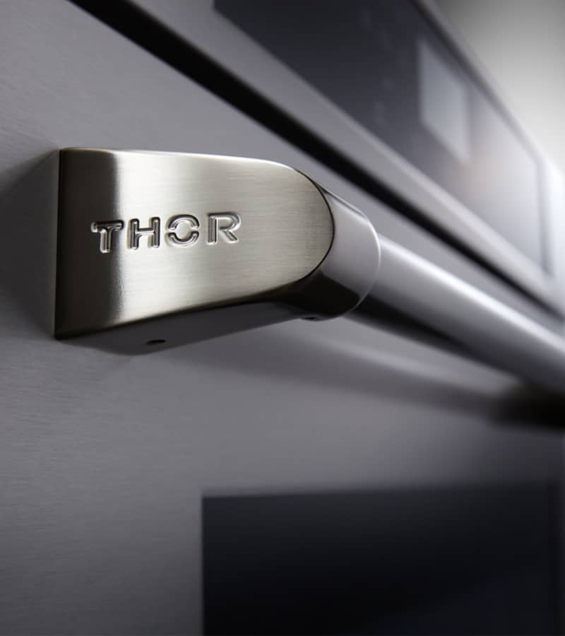 Stainless electric wall oven handle detail with THOR logo and curved grip
