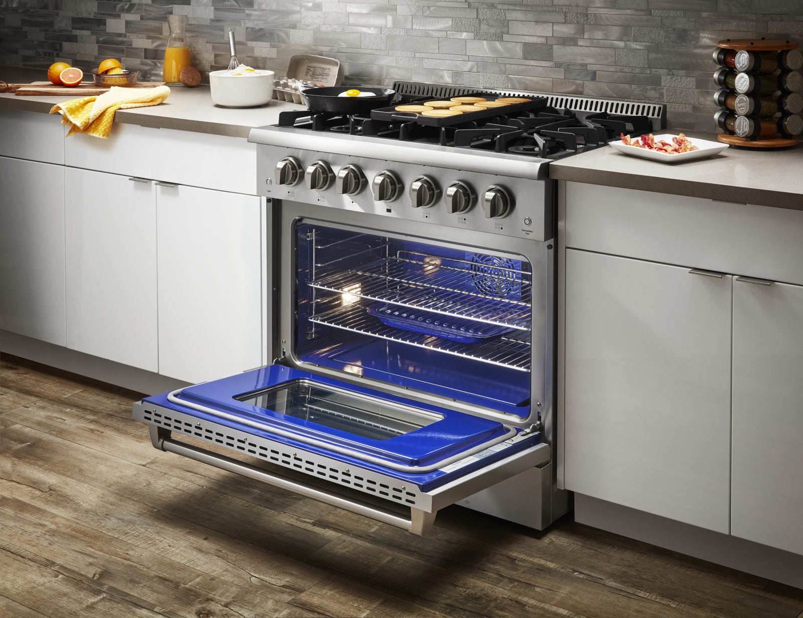 Stainless steel gas range with open oven and blue-lit interior, angled front view