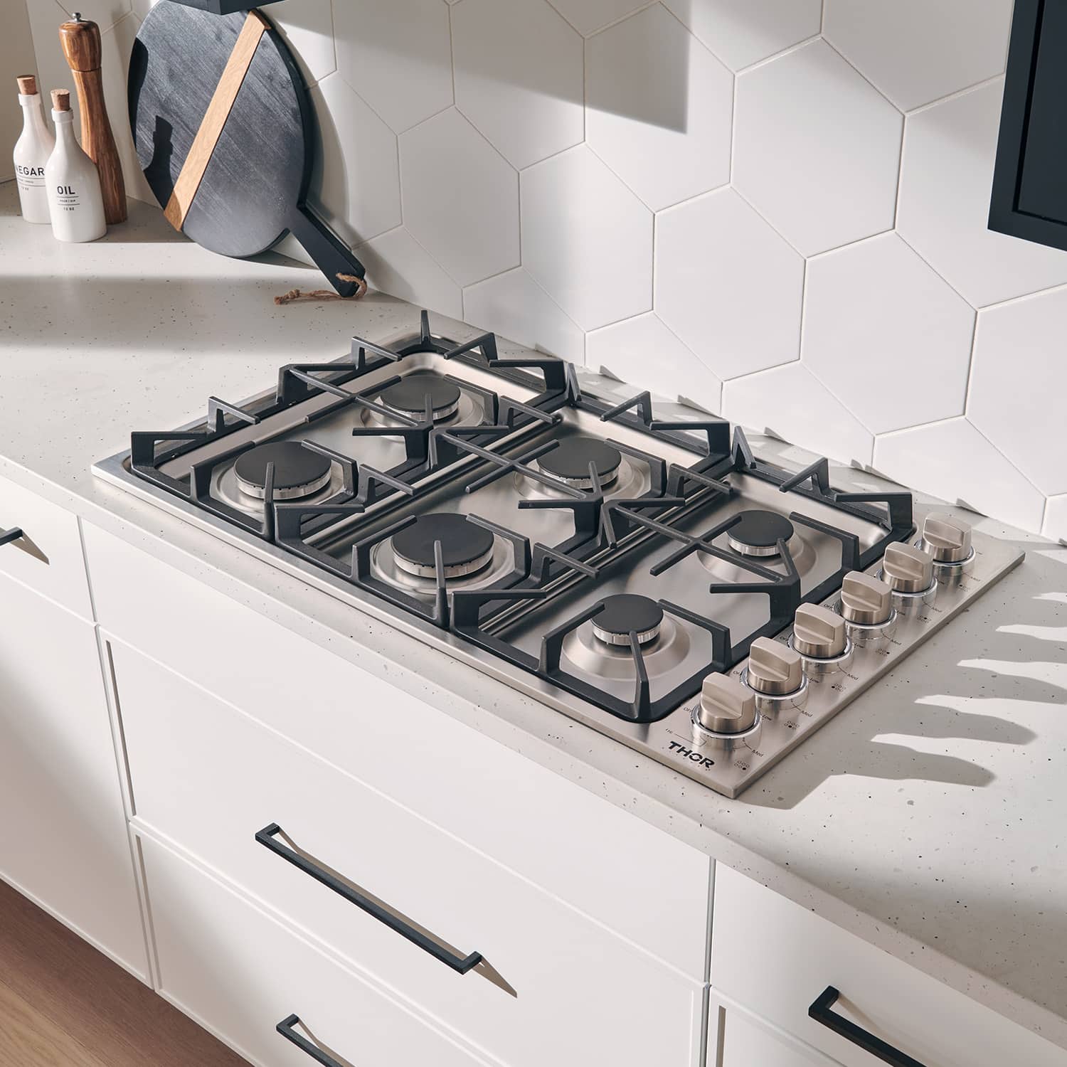 Stainless steel 6-burner gas cooktop in kitchen with pan on burner and control knobs