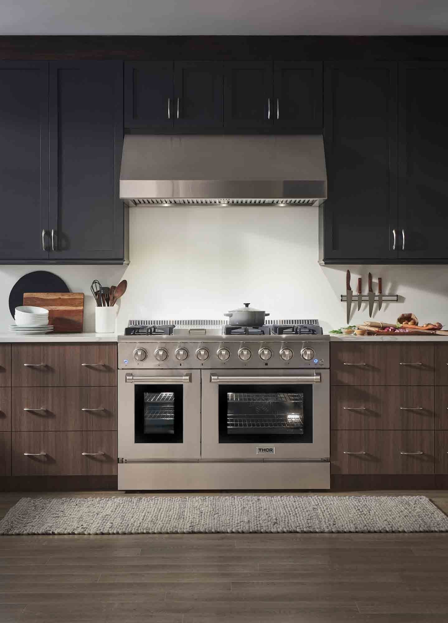 Stainless dual fuel range with chimney hood, cooktop burners, and twin oven doors
