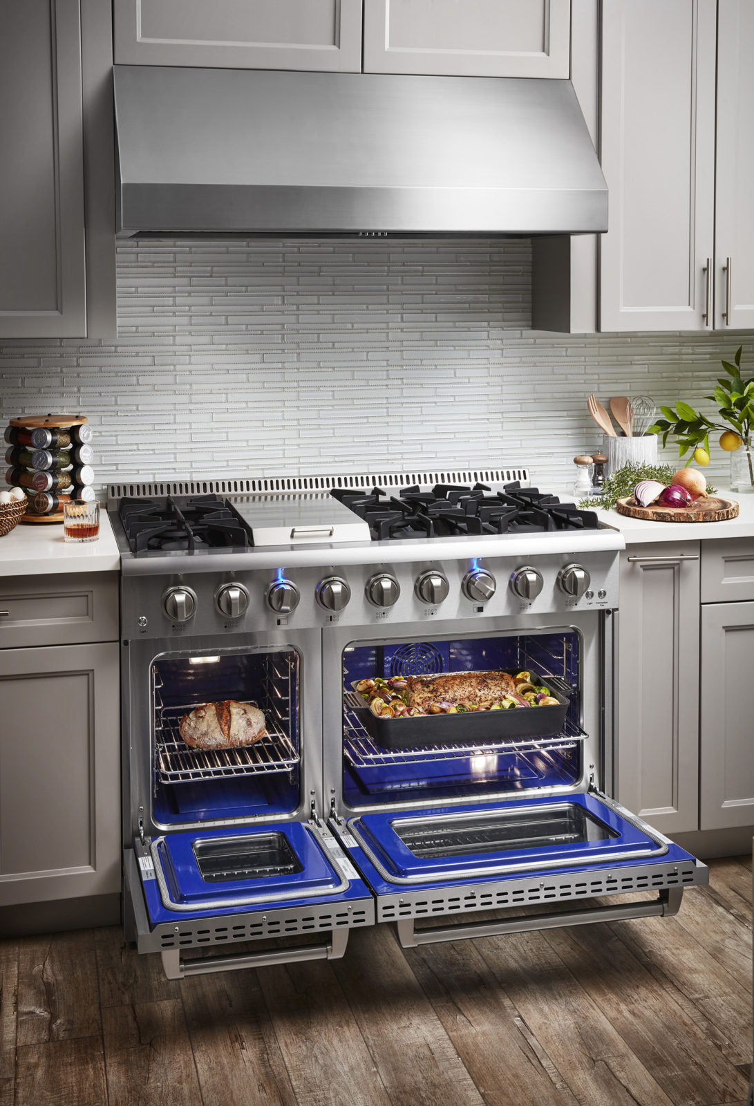 Stainless steel gas range with two open blue-lit ovens and stovetop burner grates