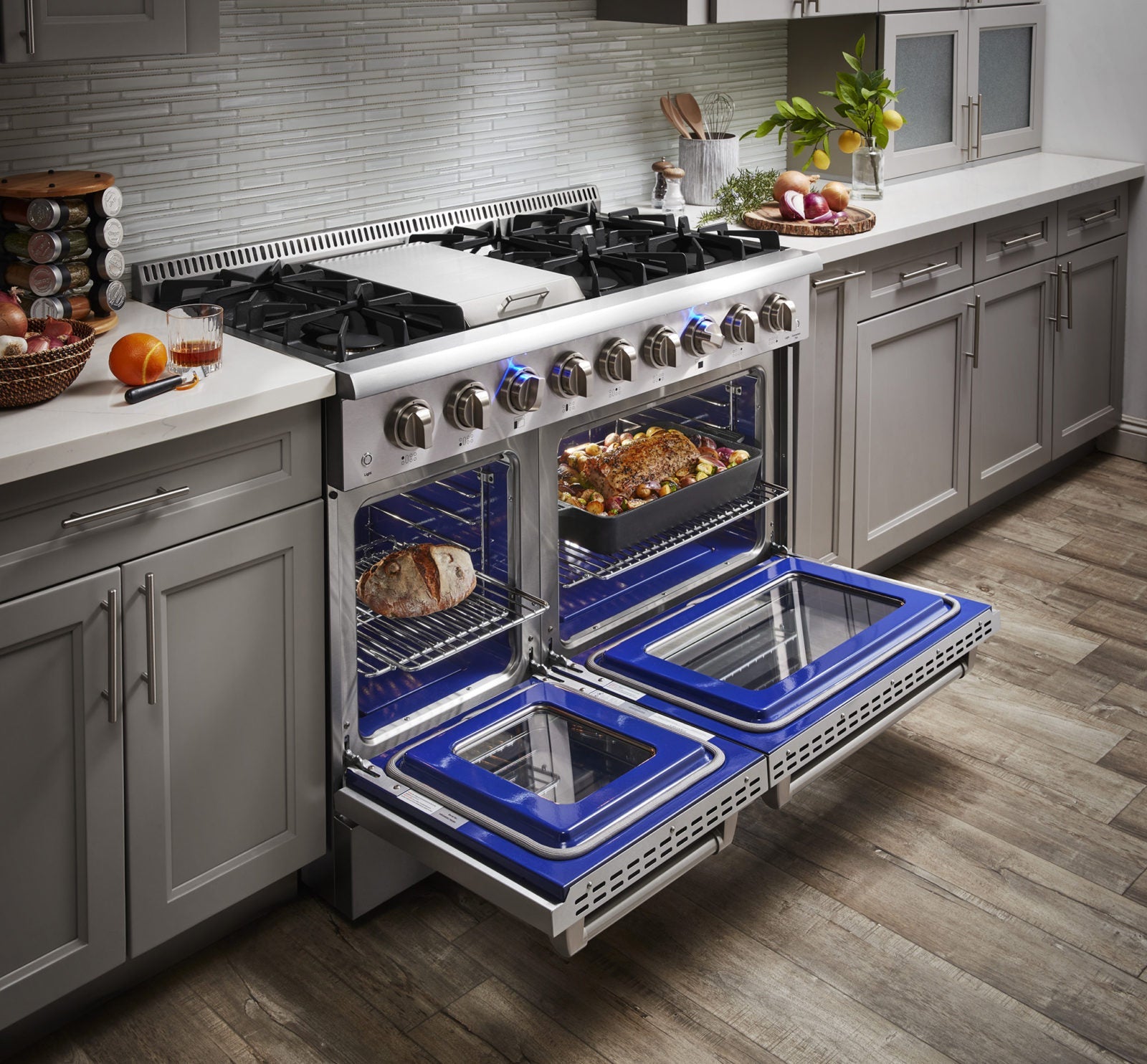 Stainless steel gas range with two open blue-lit ovens and cooking trays inside