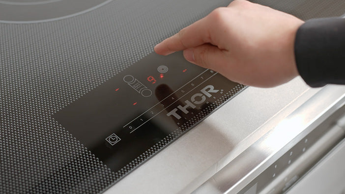 Thor electric cooktop with hand touching control panel buttons and red indicators